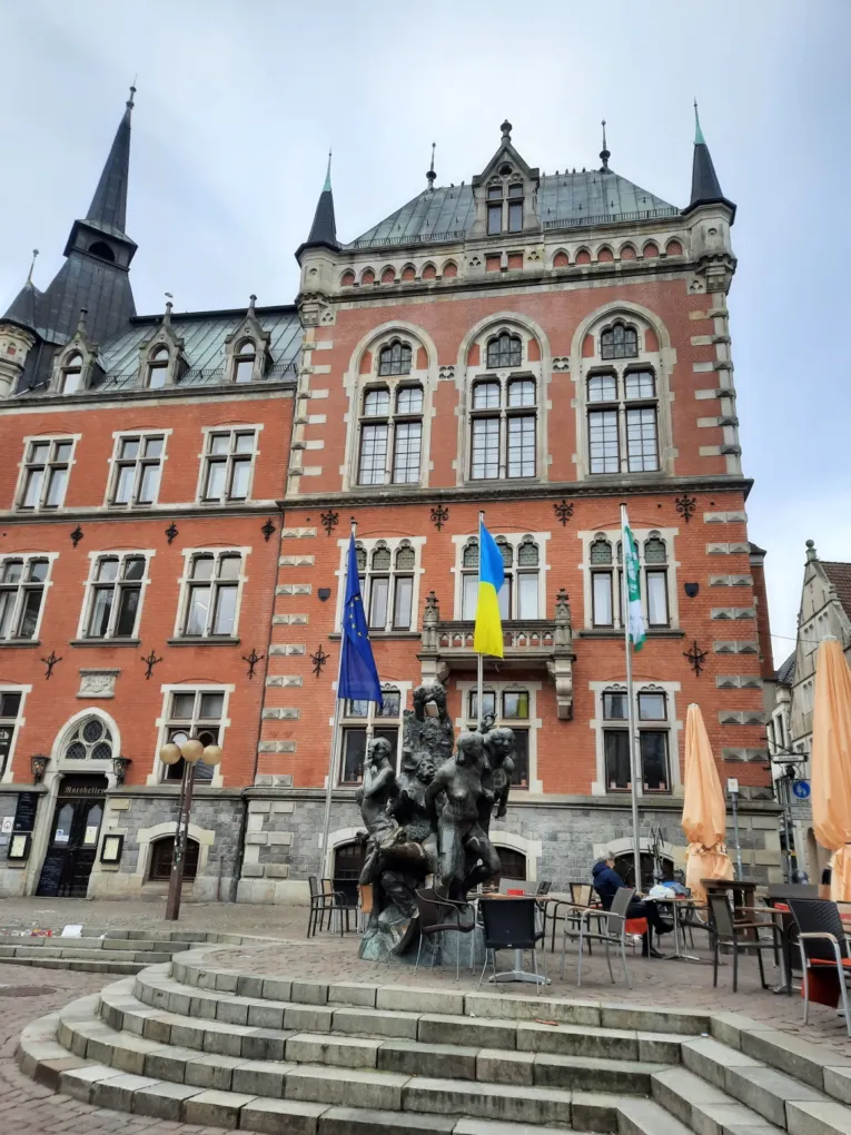 Die Mayors-for-Peace-Flagge weht vor einem Geb&auml;ude in Oldenburg neben einer Europa-Flagge und der ukrainischen Flagge im Wind.